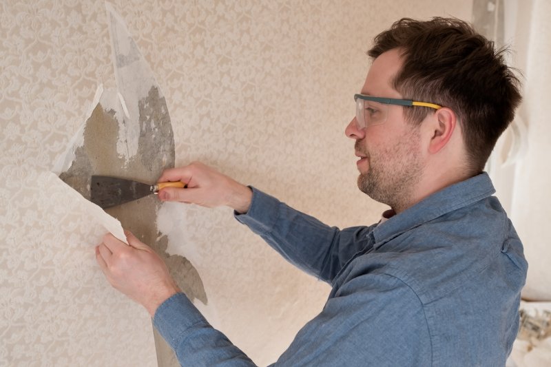Man removing old wallpaper from wall (Photo by koldunova_anna - stock.adobe.com)